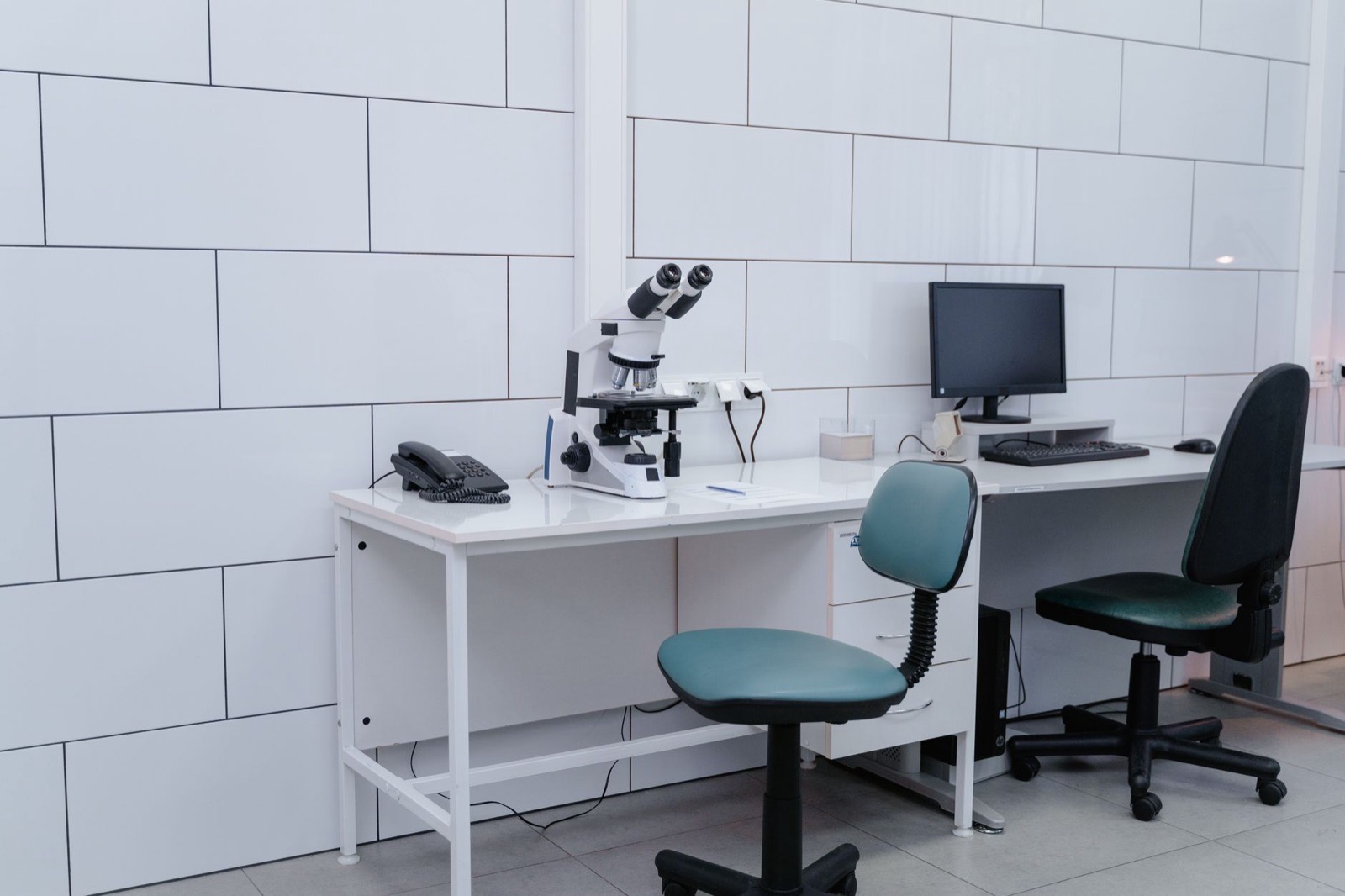 Modern laboratory with microscope, monitor, and office equipment on desk.