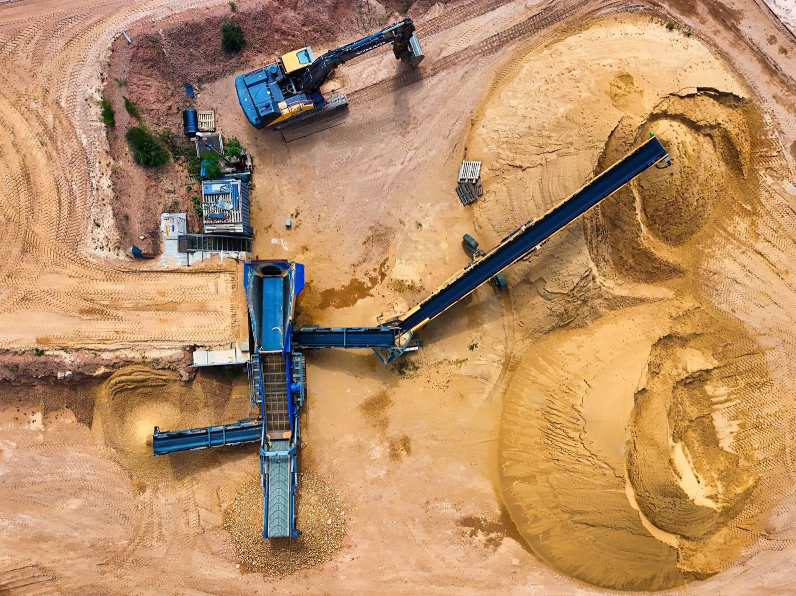 Top view of sand mining machinery and piles in outdoor quarry.