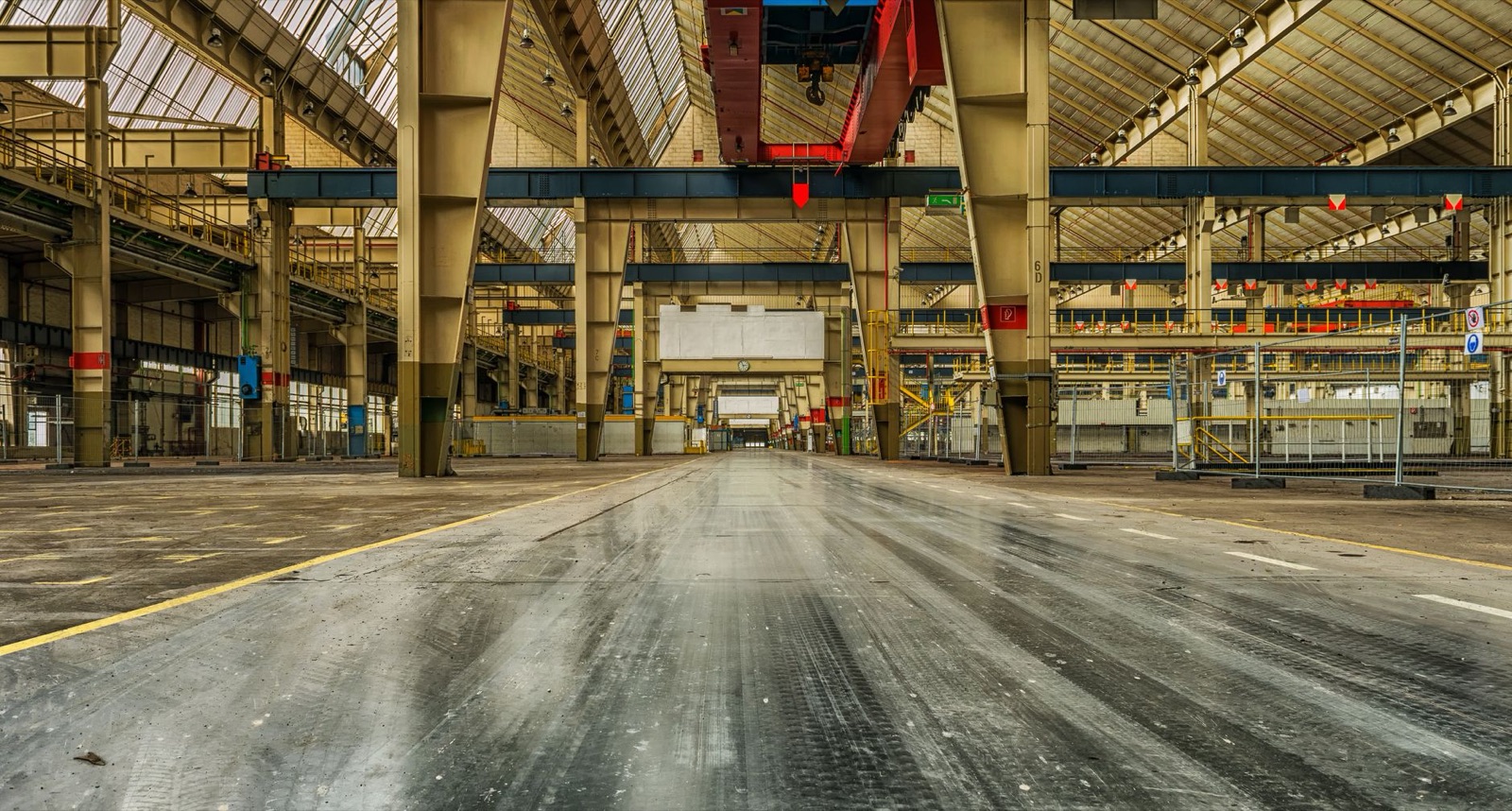 Wide view of an empty industrial warehouse with visible cranes and metal structures.