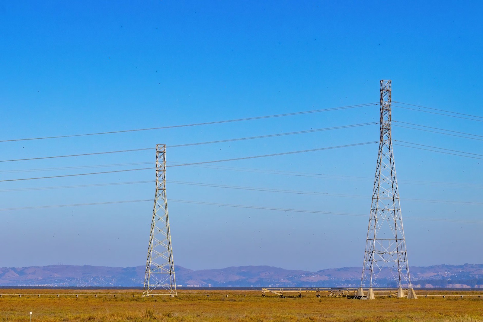 Electric towers and power lines under a clear blue sky in a natural landscape.
