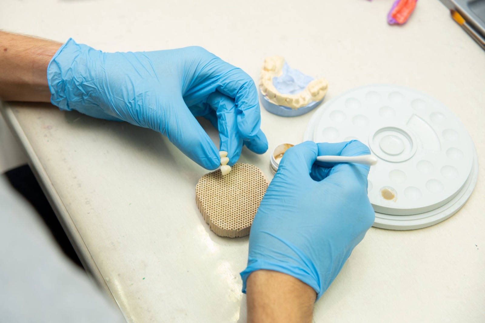 From above of crop anonymous orthodontist in latex gloves creating fake teeth for denture while sitting at table in light dental clinic