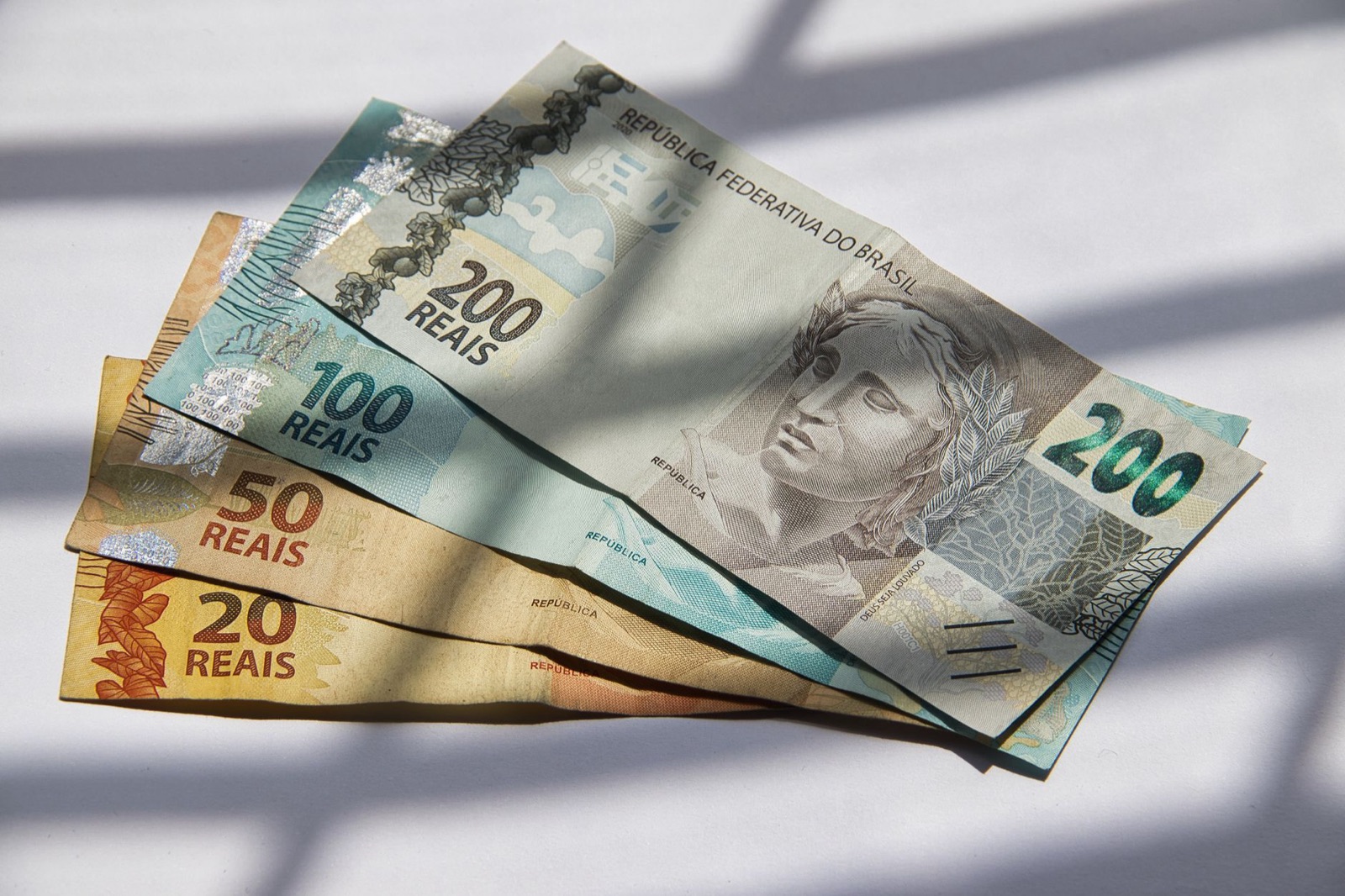 Various Brazilian real banknotes in sunlight, showcasing currency variety.