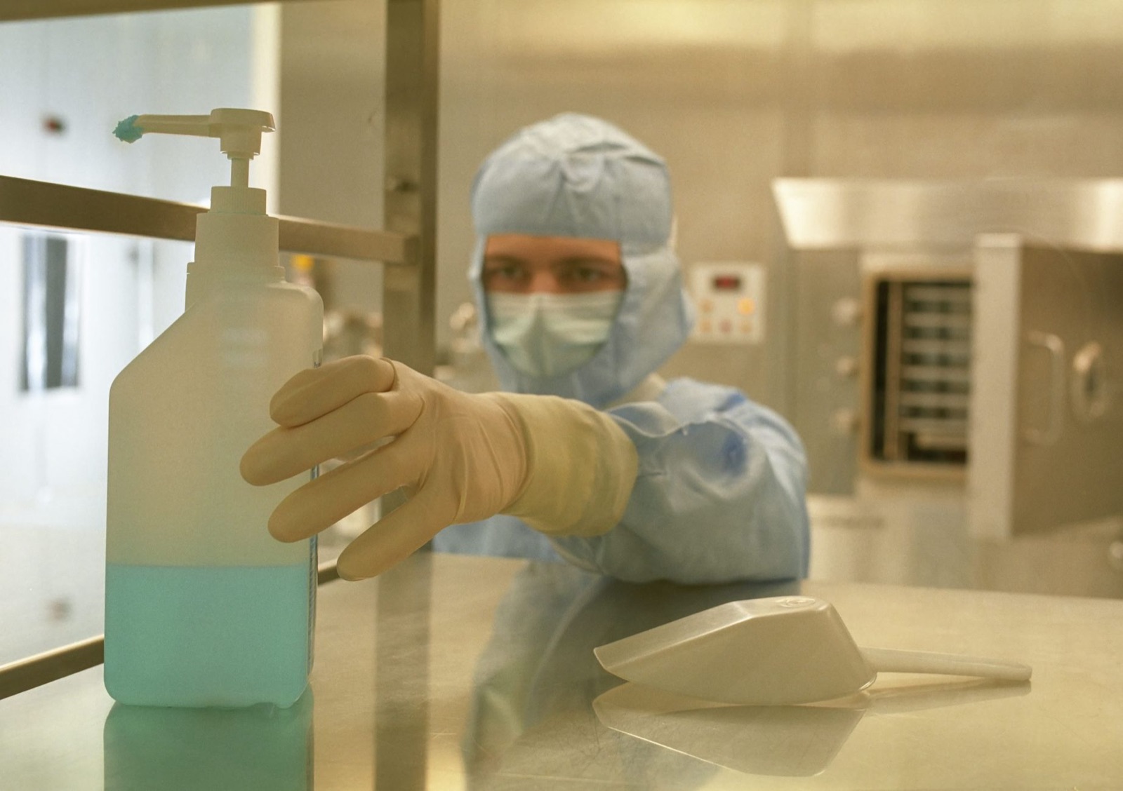 A scientist in protective gear reaching for a sanitizer bottle in a laboratory setting.
