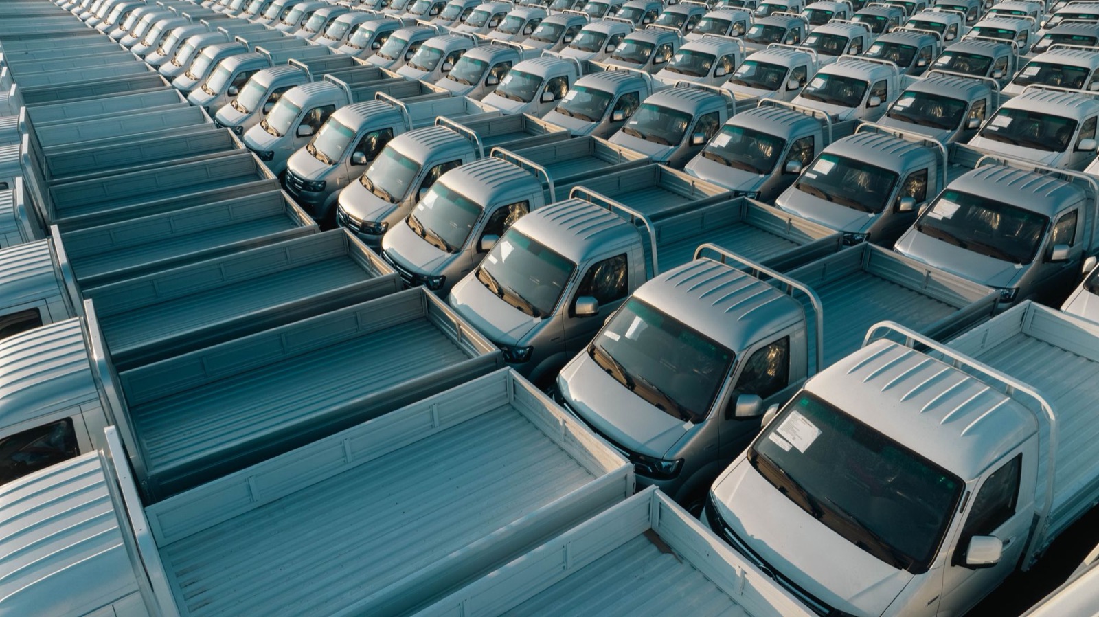 Aerial shot of multiple silver pickup trucks aligned in rows, showcasing symmetry and industrial production.